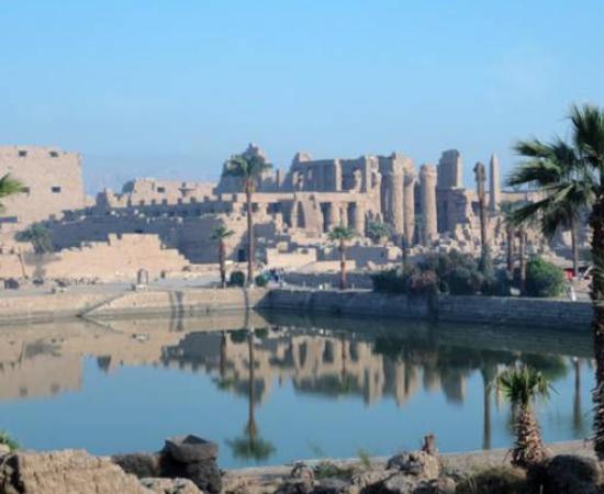 Karnak Temple Complex in Luxor, Egypt, showing the magnificent columns and sacred lake reflecting the ancient structures under clear blue skies.